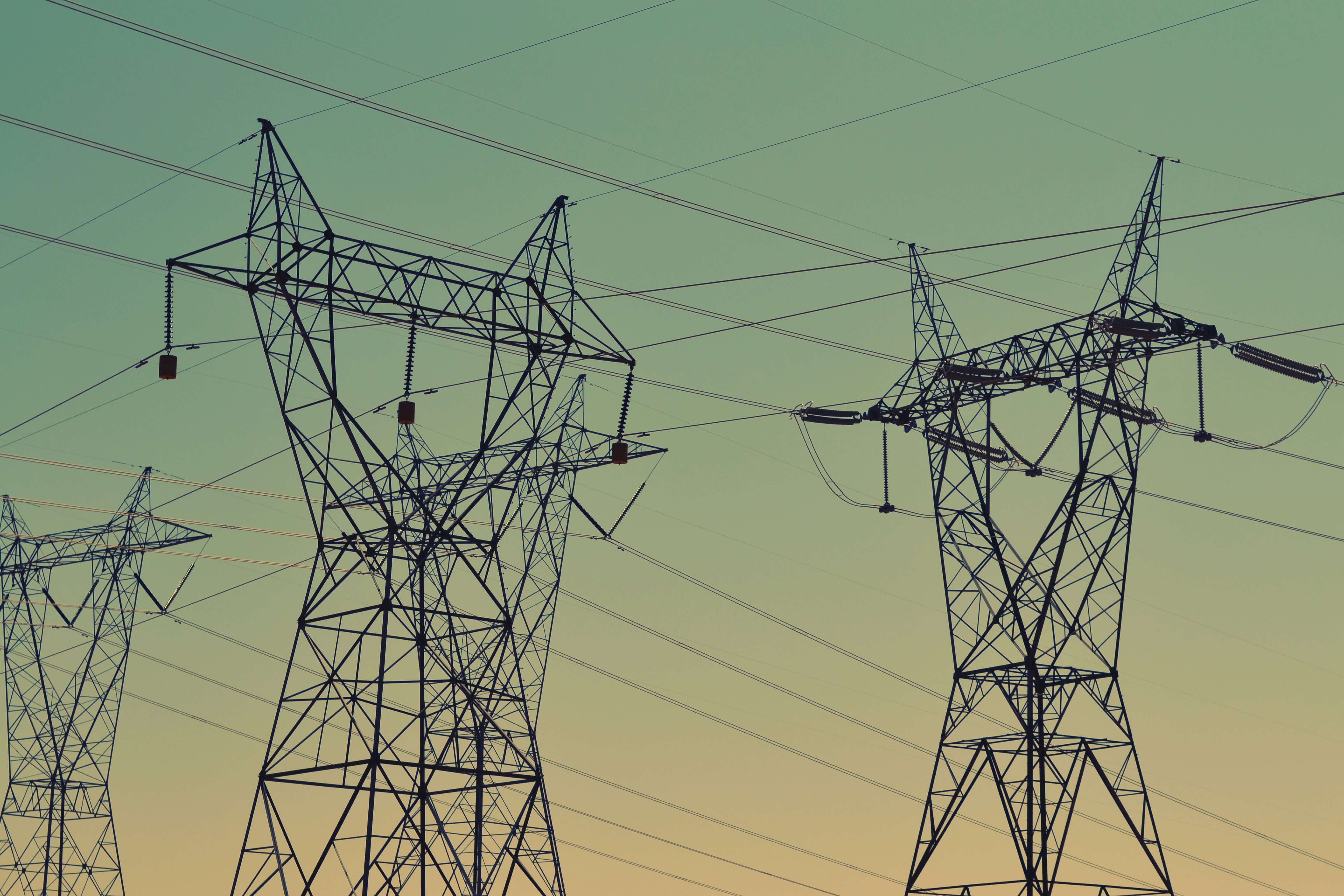 Image showing several large electrical pylons and the wires that they carry against a pale blue and pink sky