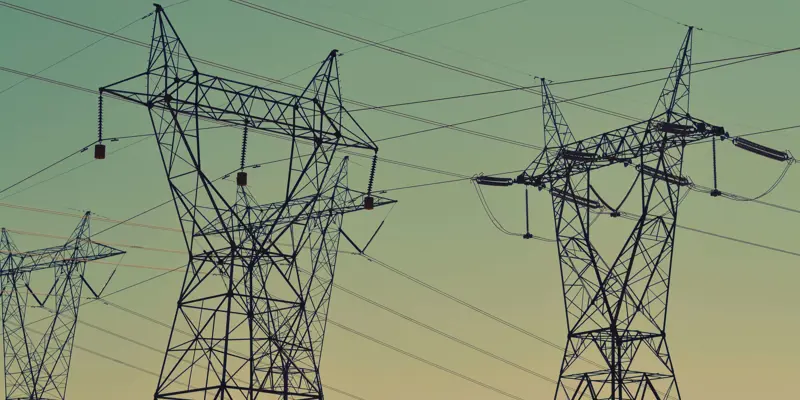 Image showing several large electrical pylons and the wires that they carry against a pale blue and pink sky