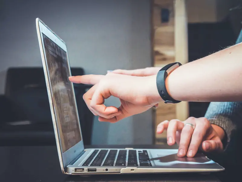 Image of two people looking at a laptop and their hands pointing at the screen