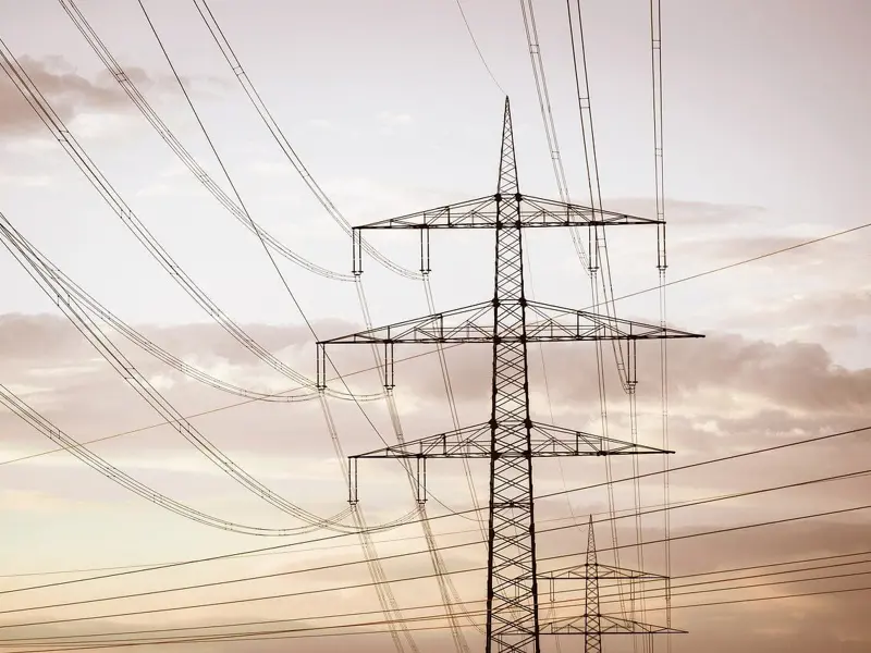 Image of an electricity pilon with wires against a pale sky